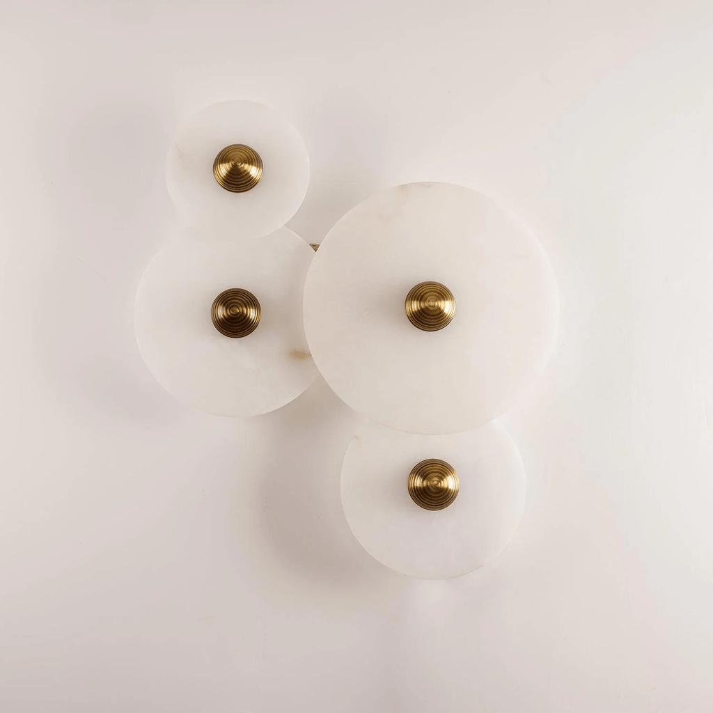 Four unlit alabaster discs clustered on a white wall, brass centres, in a loose diamond layout.
