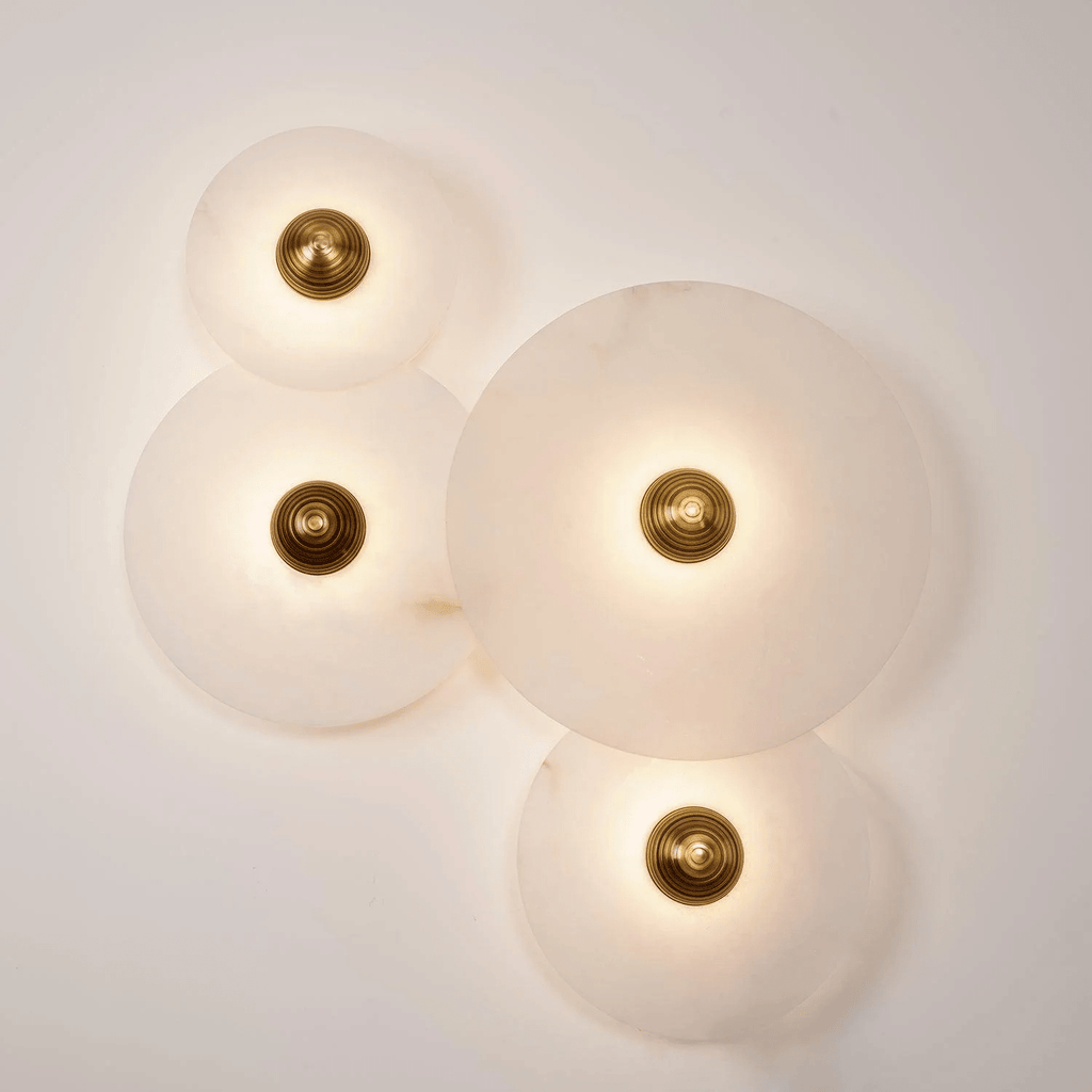 Four-disc alabaster cluster lit on a cream wall, each stone glowing around its brass centre.