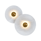 Pair of lit alabaster disc sconces with polished brass centres, glowing warm against white.