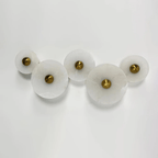 Five unlit alabaster discs in a row on a pale surface, brass centres, seen from a low angle.