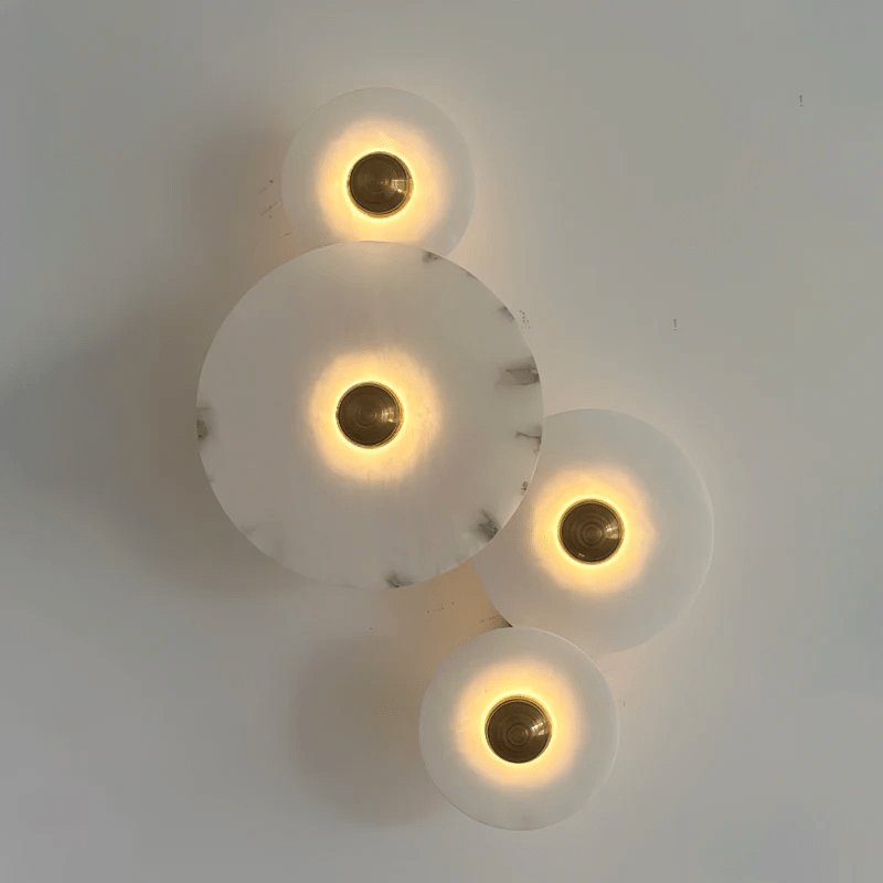 Four lit alabaster discs on a pale wall, photographed at an angle so the mounting depth shows.