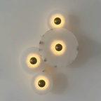 Four lit discs staggered down a pale wall, warm halos ringing each brass centre.