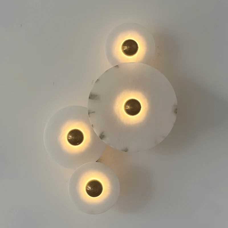 Four lit discs staggered down a pale wall, warm halos ringing each brass centre.