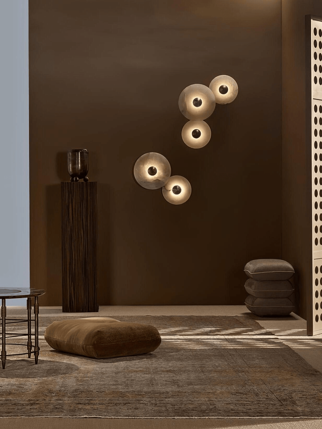 Two pairs of lit alabaster discs mounted apart on a deep brown wall in a styled living space.