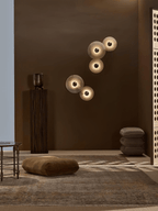 Two pairs of lit alabaster discs mounted apart on a deep brown wall in a styled living space.