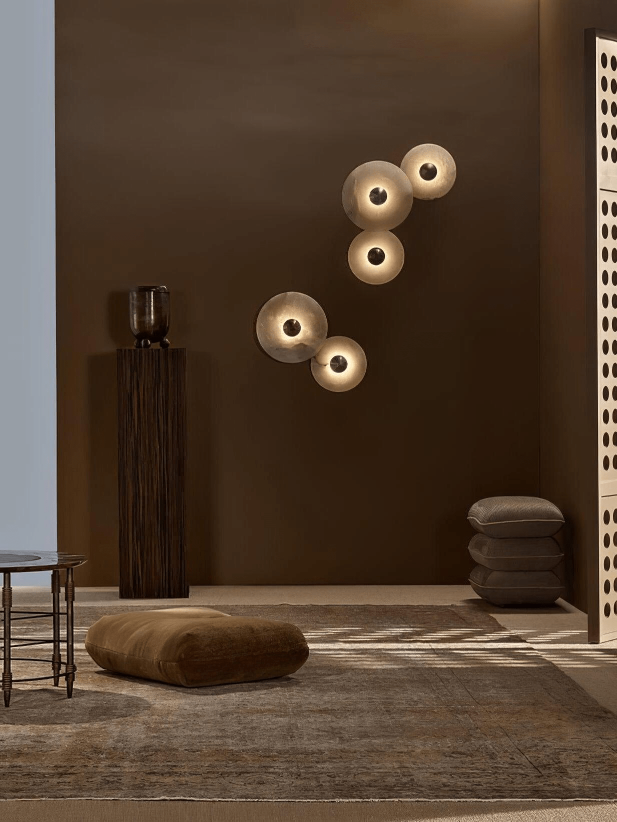 Two pairs of lit alabaster discs mounted apart on a deep brown wall in a styled living space.