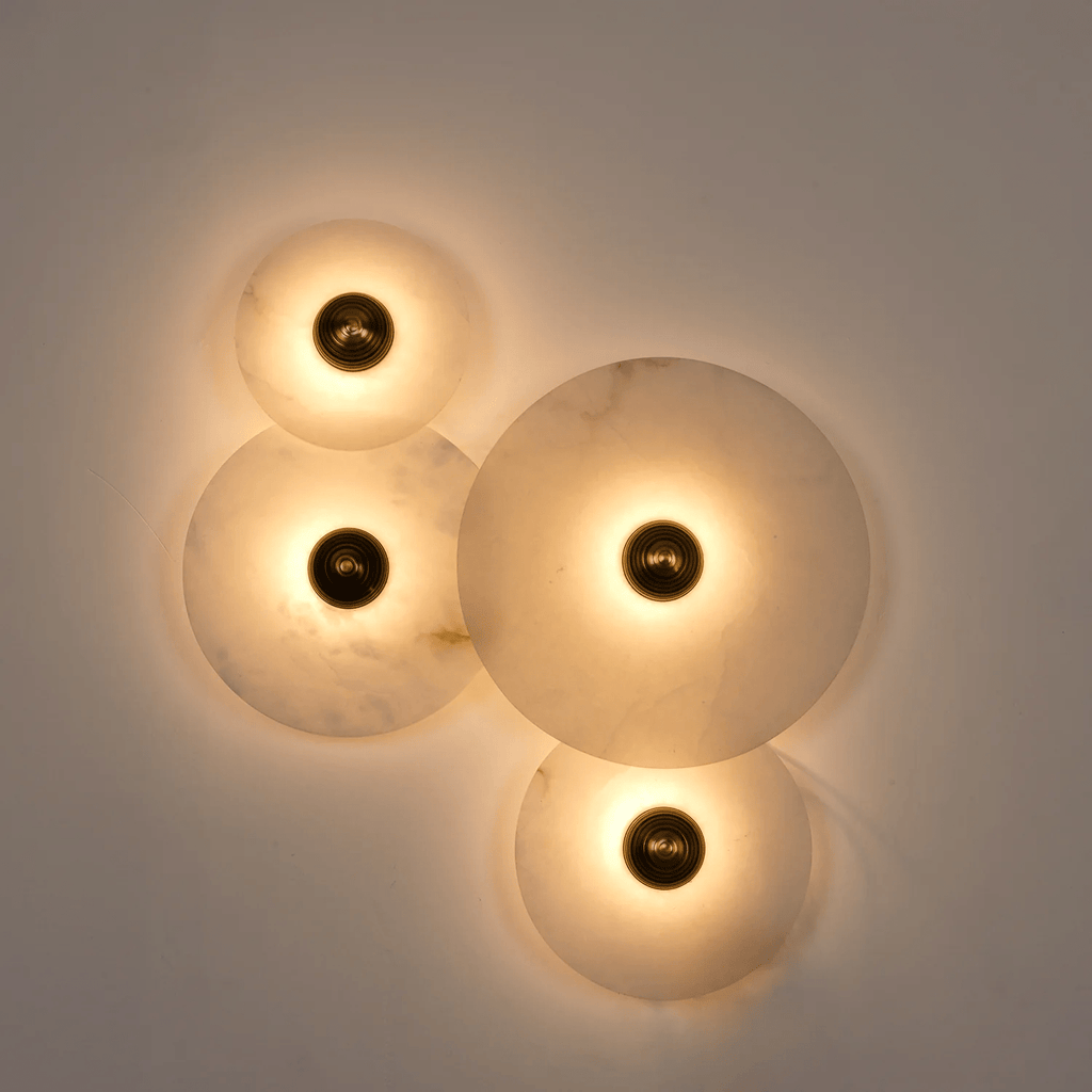 Four lit alabaster discs on a grey wall, the light spilling out in overlapping warm circles.