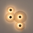 Four lit alabaster discs on a grey wall, the light spilling out in overlapping warm circles.