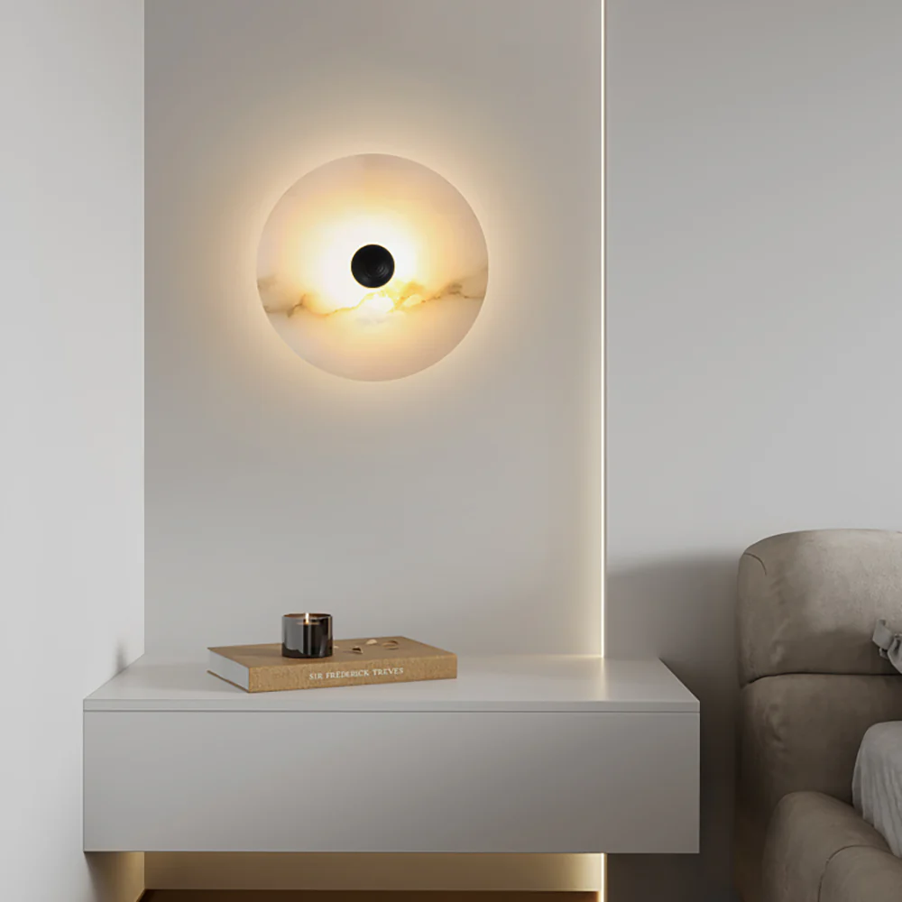 Single alabaster disc lit on a white wall above a floating console with a candle and book.