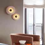 Two lit alabaster discs, one large and one small, on a taupe wall beside a balcony window.