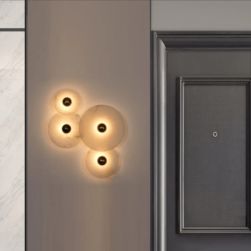 Four-disc alabaster cluster lit on a grey wall next to a dark panelled door.