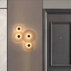 Four-disc alabaster cluster lit on a grey wall next to a dark panelled door.