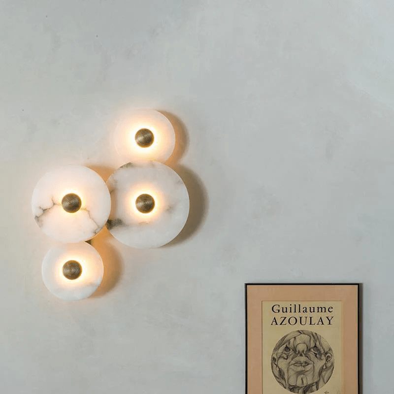Four lit alabaster discs on a pale plaster wall, hung above a framed poster.