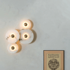 Four lit alabaster discs on a pale plaster wall, hung above a framed poster.