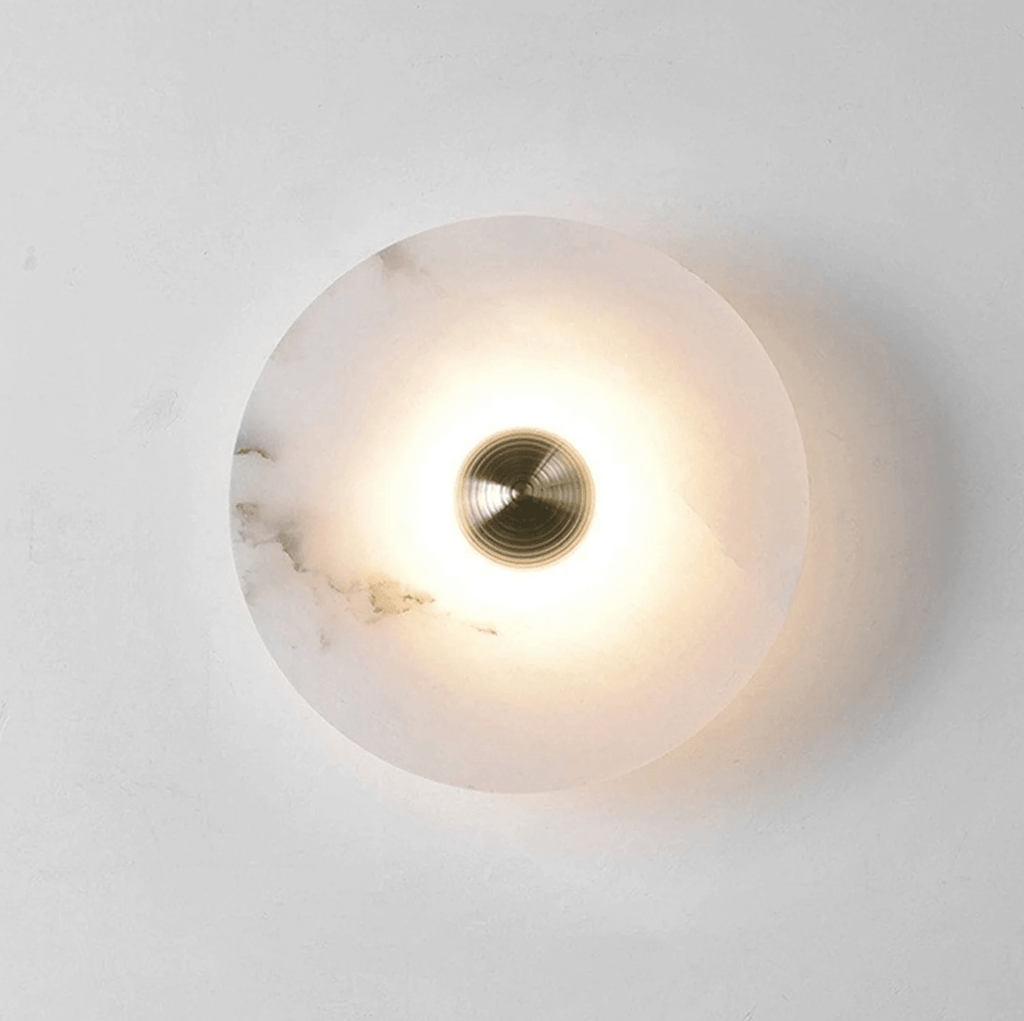 Single alabaster disc lit on a white wall, the glow ringing the brass centre and fading outward.