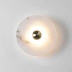 Single alabaster disc lit on a white wall, the glow ringing the brass centre and fading outward.
