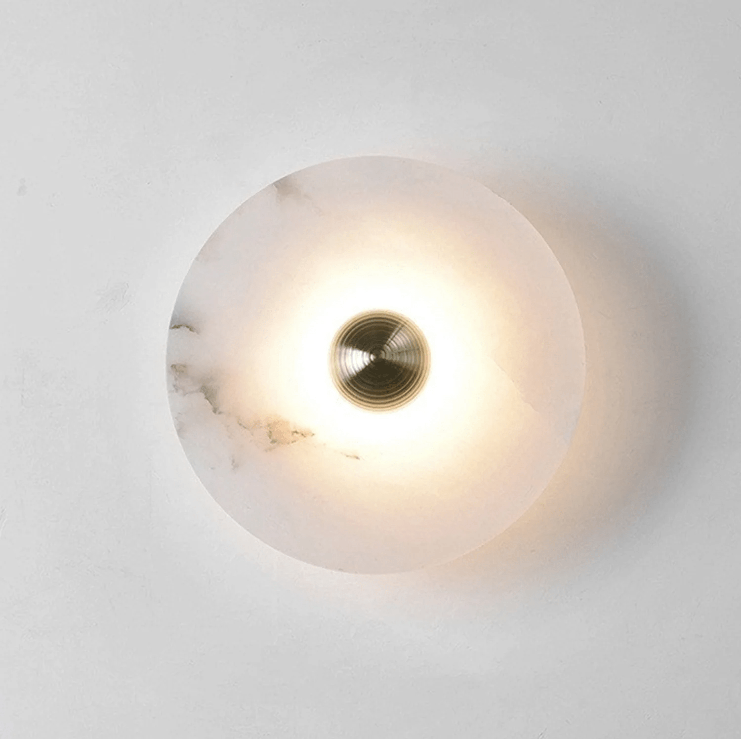 Single alabaster disc lit on a white wall, the glow ringing the brass centre and fading outward.