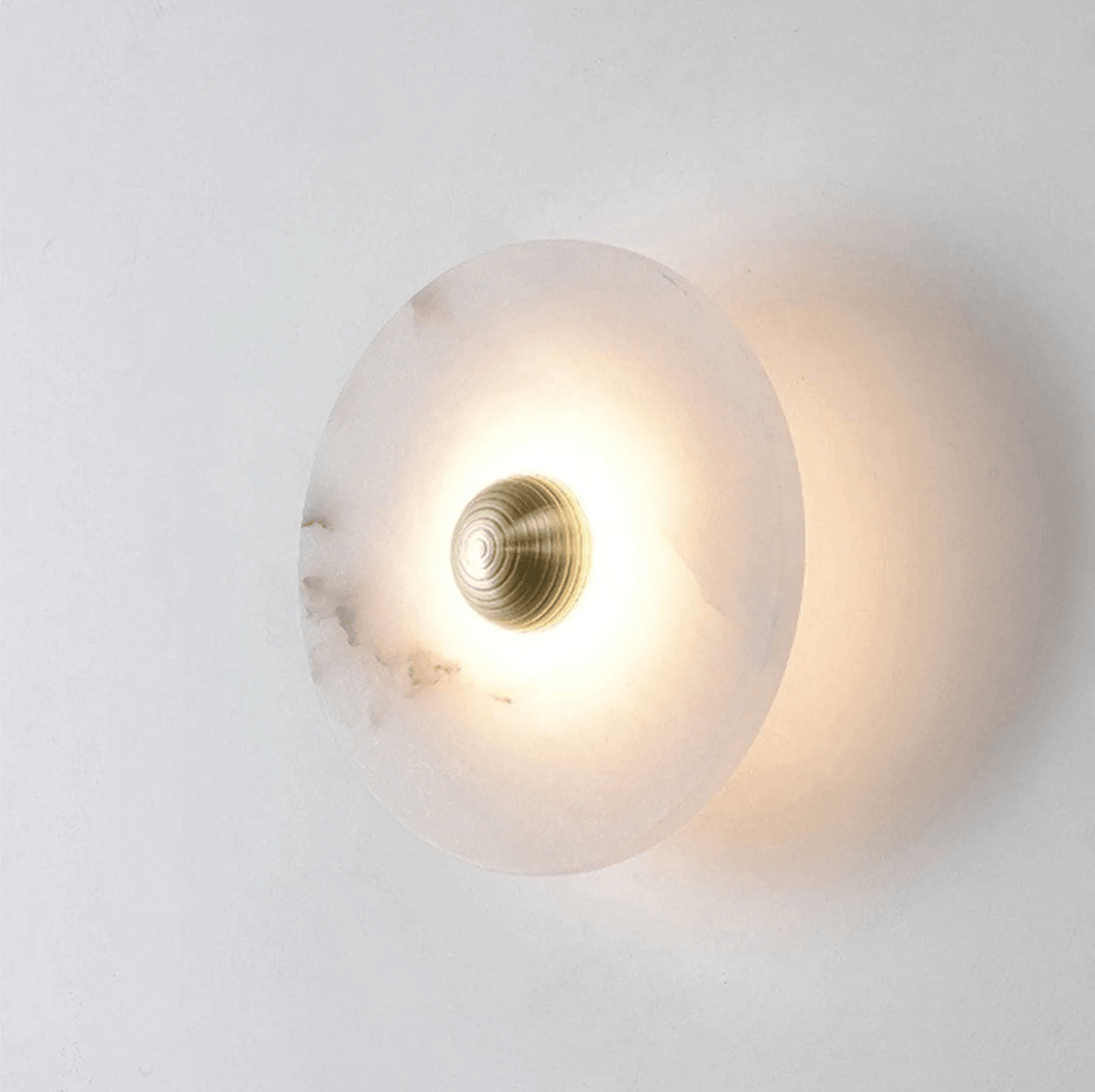 Single lit alabaster disc seen from the side, its glow throwing a soft halo onto the wall.