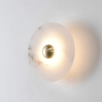 Single lit alabaster disc seen from the side, its glow throwing a soft halo onto the wall.