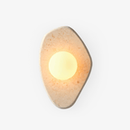 Beige carved-marble wall light with a glowing white glass orb from Clérachic, on a plain white studio background.