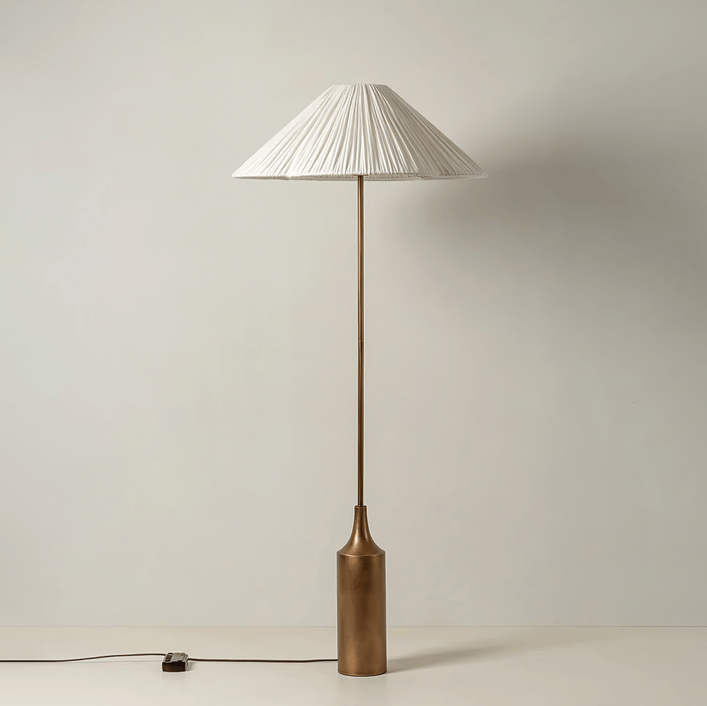 Shown full length on a plain white background, a Clérachic pleated white cone-shade floor lamp sits on its brass bottle base.