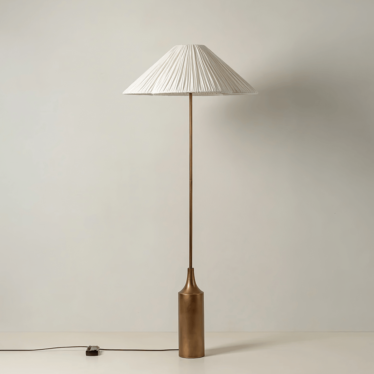 Shown full length on a plain white background, a Clérachic pleated white cone-shade floor lamp sits on its brass bottle base.