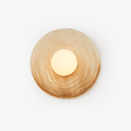 A ridged terra-beige ceramic wall sconce from Clérachic on a white studio background, its opal globe glowing warm off-centre.