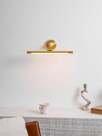 This Clérachic wall sconce in gold glows above a table with a small jug, an ornate candlestick and a stack of books.