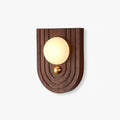 Koyan wall light with an arched, ridged walnut backplate, alabaster globe and small brass knob below.