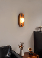 Oval Koyan wall light lit beside a black leather sofa and a side table of dried flowers.