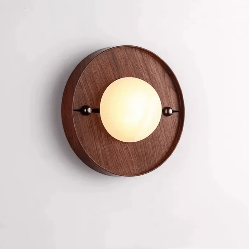 Round walnut backplate version of the Koyan wall light, alabaster globe lit between two dark ball fittings.