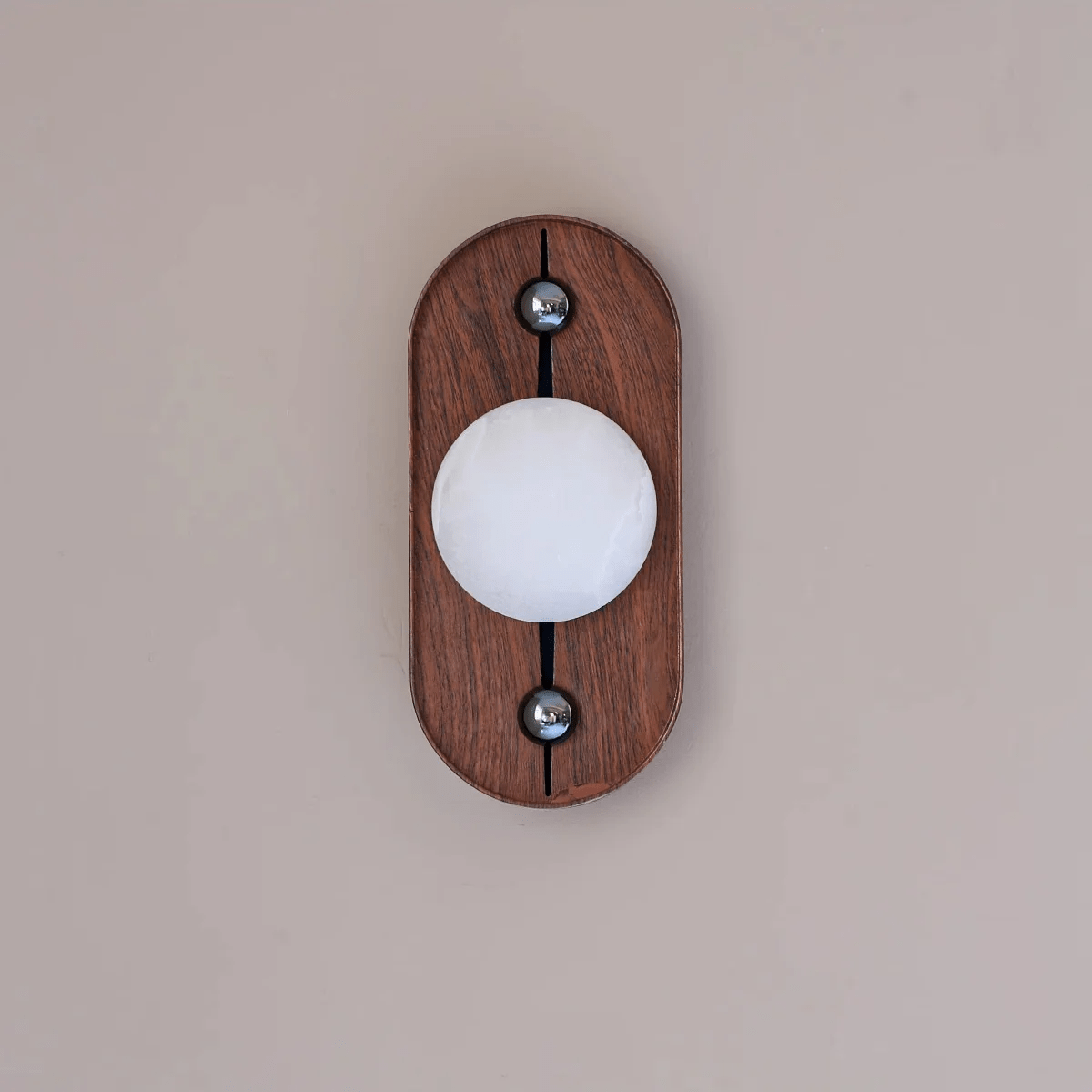 Oval Koyan wall light unlit on a blush wall, straight on, the alabaster globe's veining clearly visible.