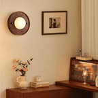 Round Koyan wall light lit above a walnut sideboard with roses, next to a framed picture.