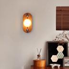 Oval Koyan wall light lit in a living room, seen square-on above a reed diffuser and sideboard.