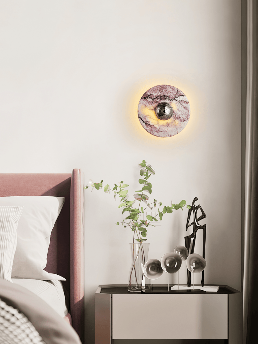 A lit Clérachic wall light glows above a mauve upholstered headboard, beside a glass vase of eucalyptus stems and a figurine.