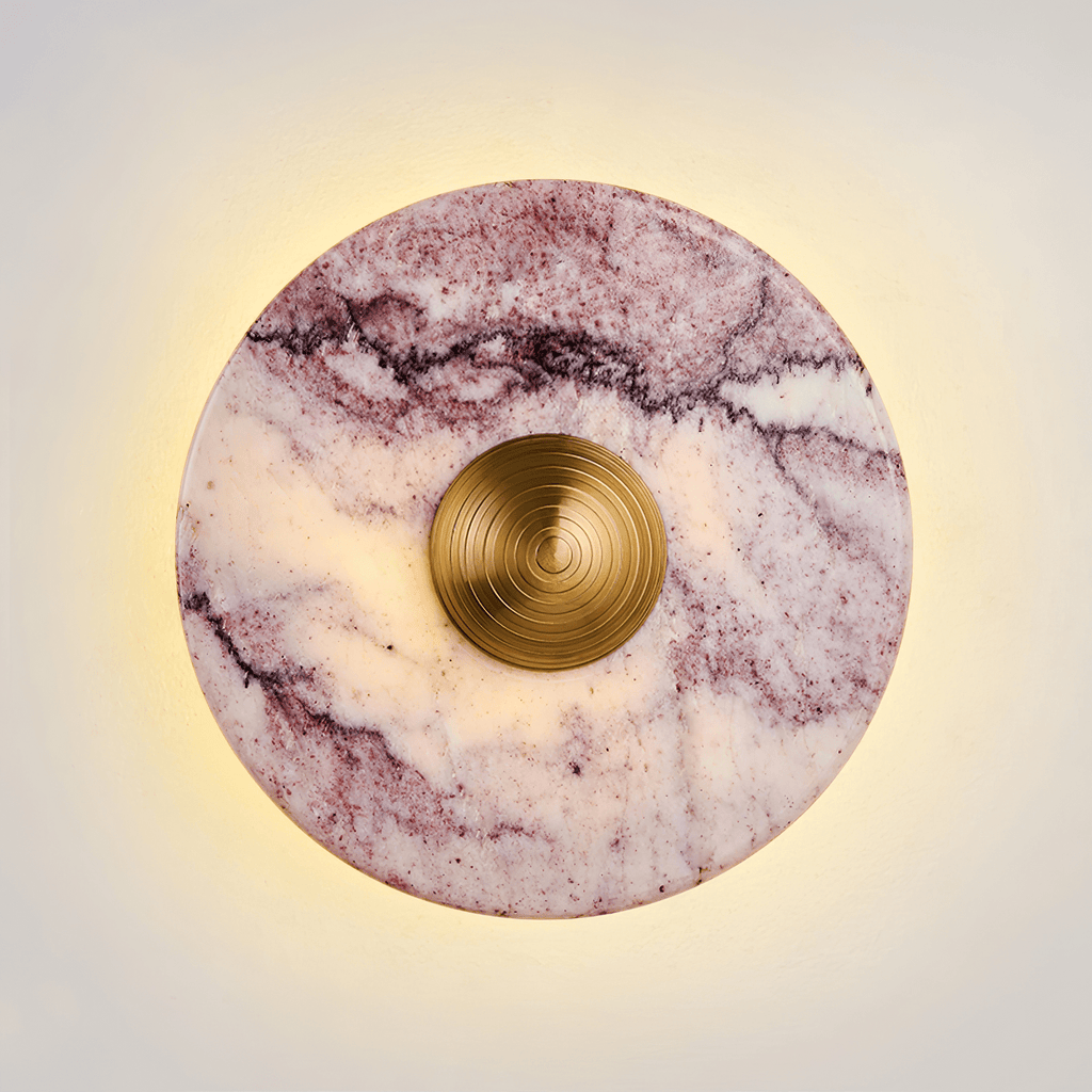 Close-up of a Clérachic wall light in purple-veined marble, its gold ridged centre knob glowing warm against a soft backlit halo.