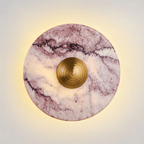 Close-up of a Clérachic wall light in purple-veined marble, its gold ridged centre knob glowing warm against a soft backlit halo.