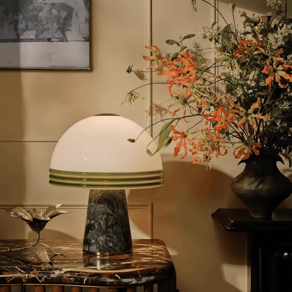 A large arrangement of orange flowers sits beside the Clérachic dome table lamp, lit on a marble-top console table.