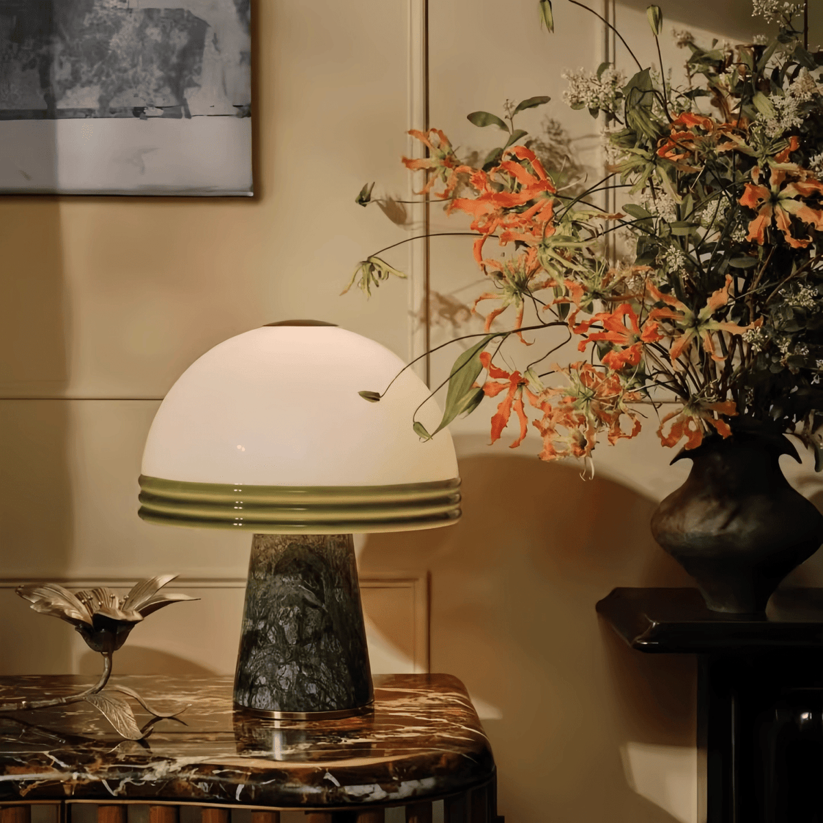 A large arrangement of orange flowers sits beside the Clérachic dome table lamp, lit on a marble-top console table.