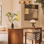 Beneath a pendant light fixture in a study, the Clérachic dome table lamp lights a curved wood credenza framed by art.
