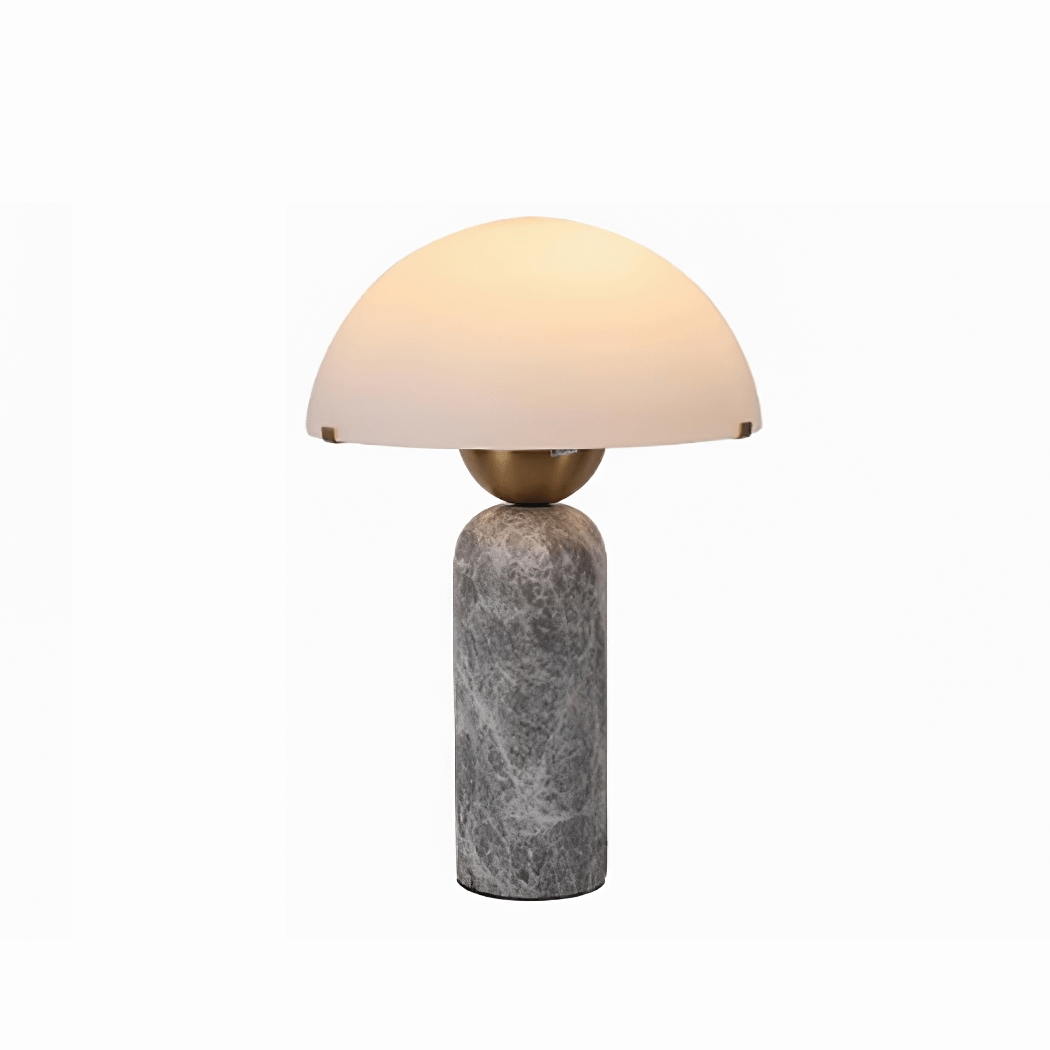 Studio shot of a Clérachic dome table lamp with a grey marble base and gold sphere stem, lit against white.