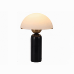 Studio shot of a Clérachic dome table lamp with a glossy black marble base, its dome shade softly lit on white.