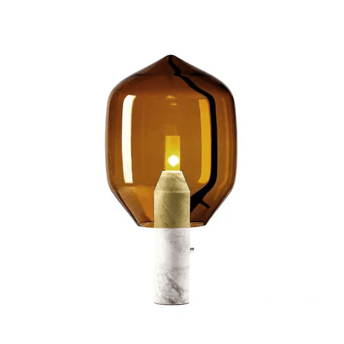 Clérachic's amber-glass table lamp on a white marble base, lit against a plain white background with its switch visible.