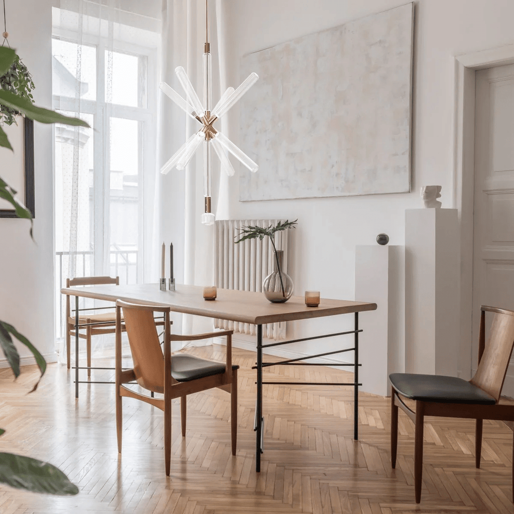 A Clérachic pendant with crystal rods bursting from a gold joint, lit above a wood dining table by tall windows.