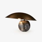 A wide brass dome rests on a grey and black marble sphere, the Clérachic table lamp lit from beneath the shade.