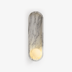 A Clérachic marble wall light in an oval niche shape, its frosted opal sphere glowing softly on a plain background.