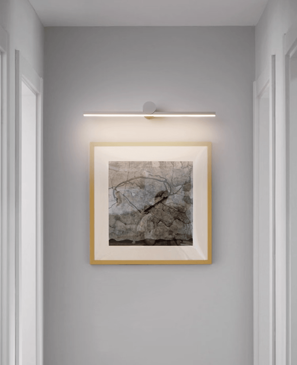 A lit Clérachic wall light glows above a gold-framed abstract print in a hallway.