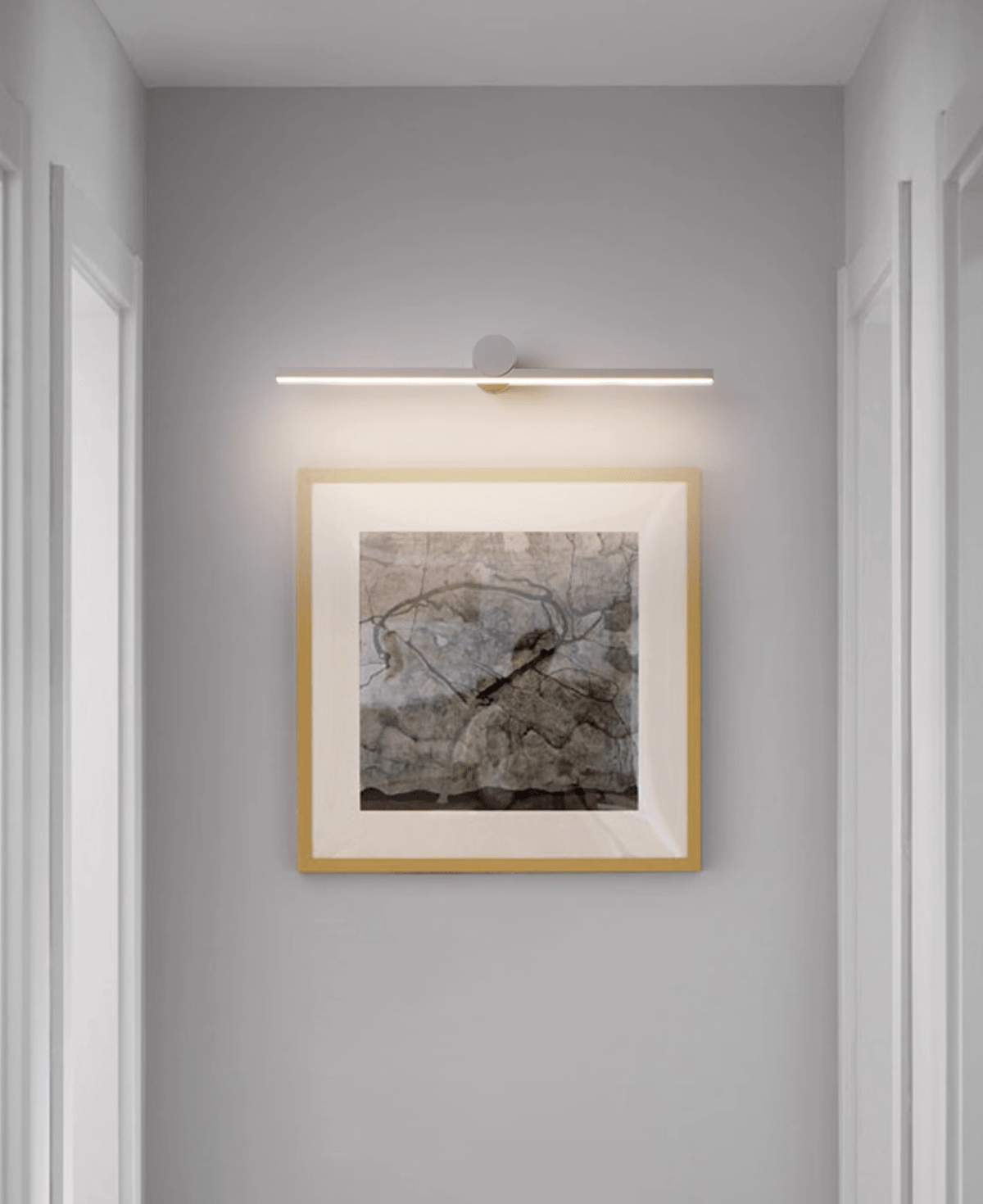 A lit Clérachic wall light glows above a gold-framed abstract print in a hallway.