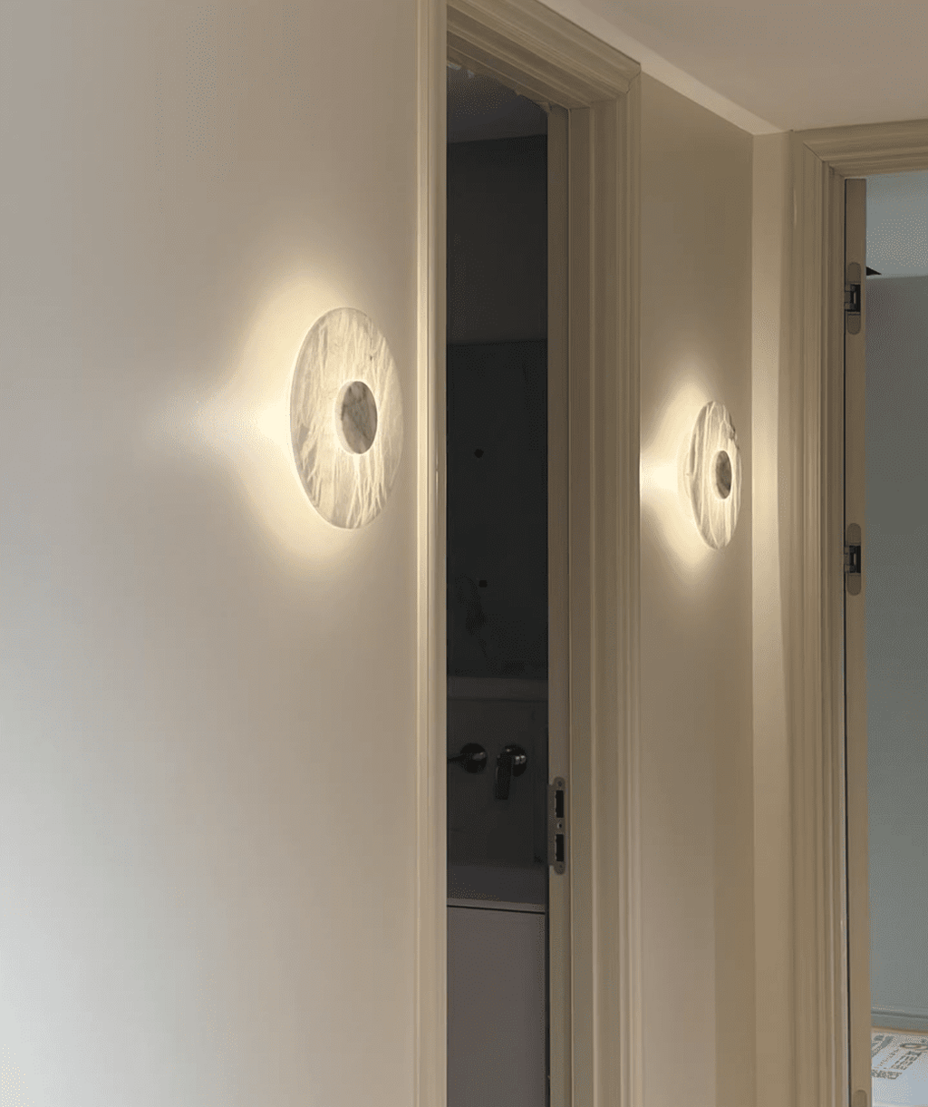 Two Clérachic alabaster wall lights glow along a hallway wall beside two panelled doors leading to further rooms.