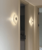 Two Clérachic alabaster wall lights glow along a hallway wall beside two panelled doors leading to further rooms.